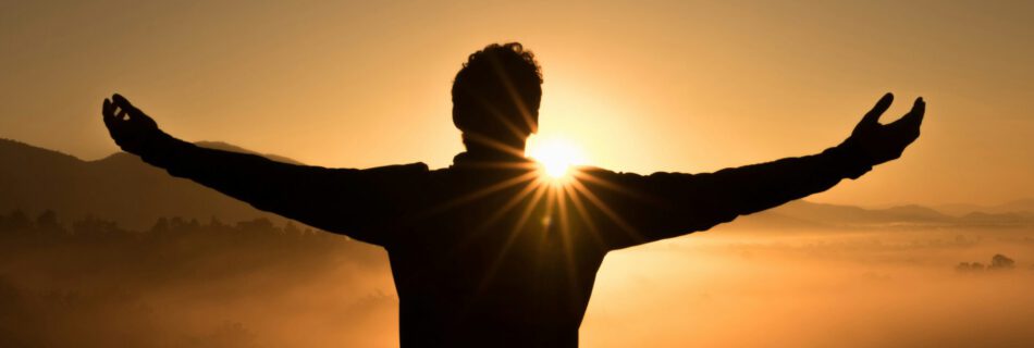 Person mit erhobenen Armen bei Sonnenuntergang
