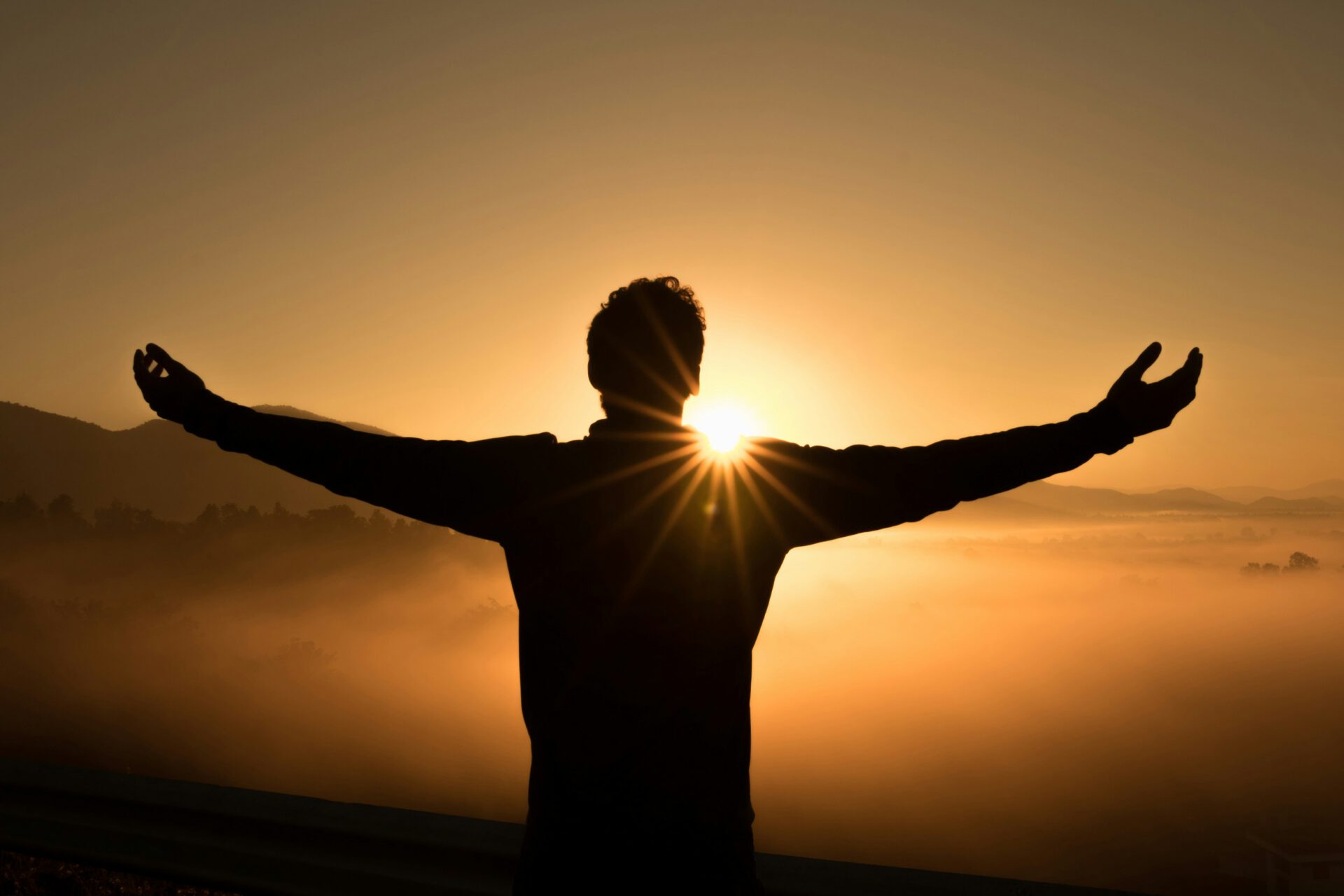 Person mit erhobenen Armen bei Sonnenuntergang